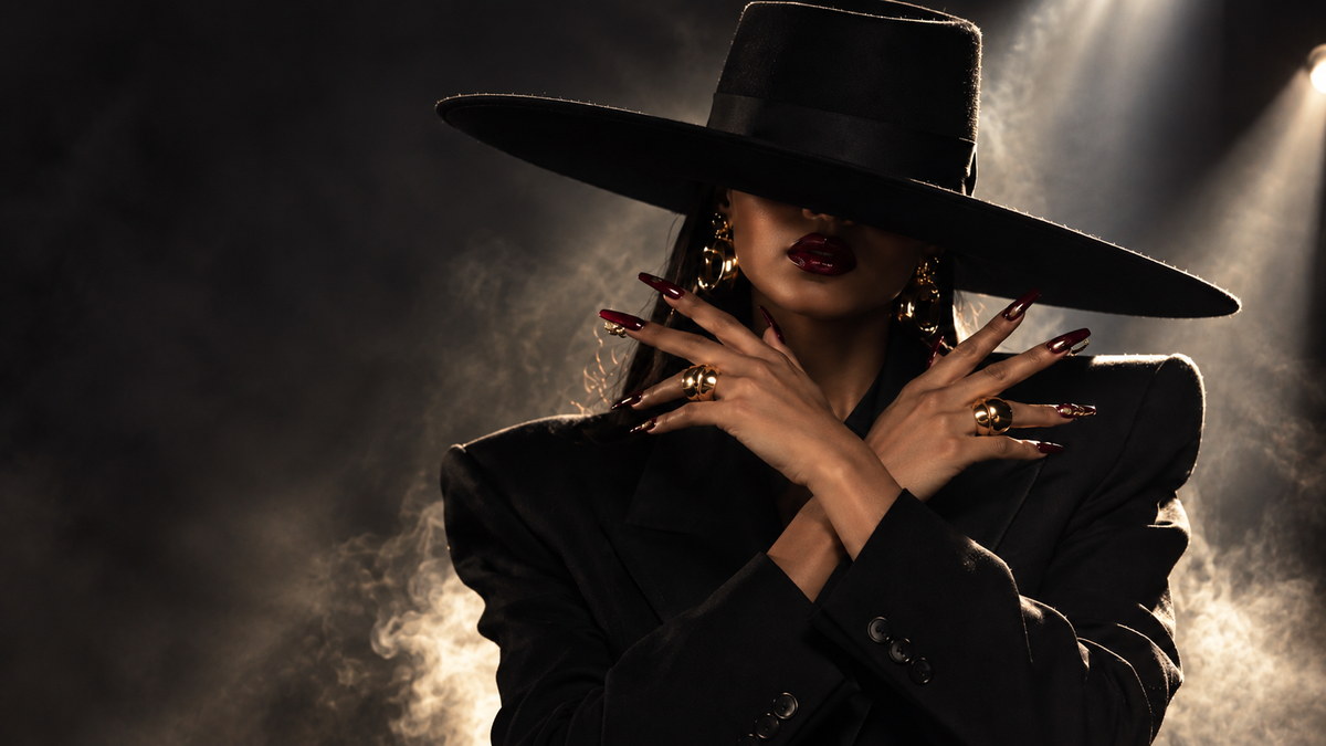 ROVIA campaign: burgundy and gold nails, sculptural black tailoring and an oversized black hat in smoke